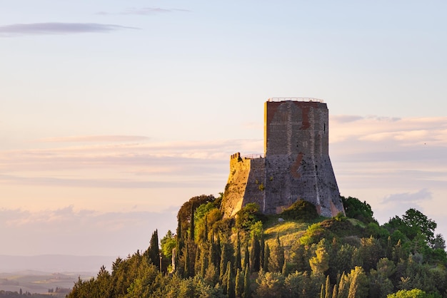 写真 イタリア、トスカーナの中世の村と要塞ロッカドルチア夕暮れ時のユニークな景色劇的な空を背景に岩の崖の上に建つ石の塔