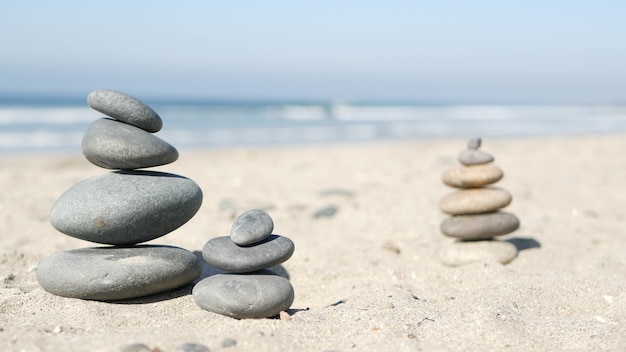 Bilanciamento della roccia sulla spiaggia dell'oceano, pietre impilate dalle onde dell'acqua di mare. piramide di ciottoli sulla riva sabbiosa. mucchio o mucchio stabile con messa a fuoco morbida con bokeh, primo piano. equilibrio zen, minimalismo, armonia e pace