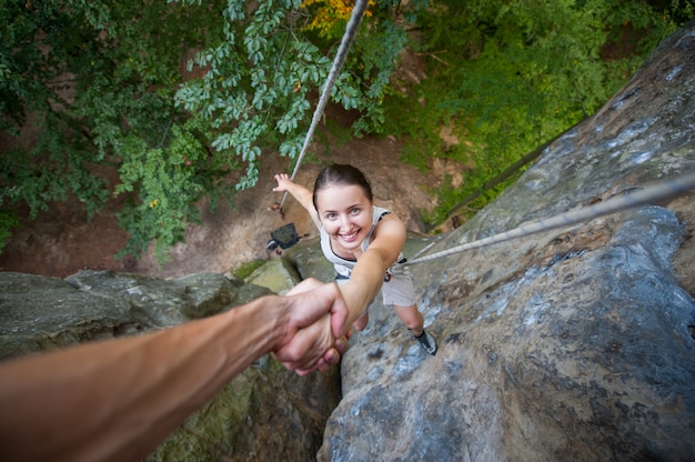 Rock climber is holding a sporty female climber by hand on a rocky wall