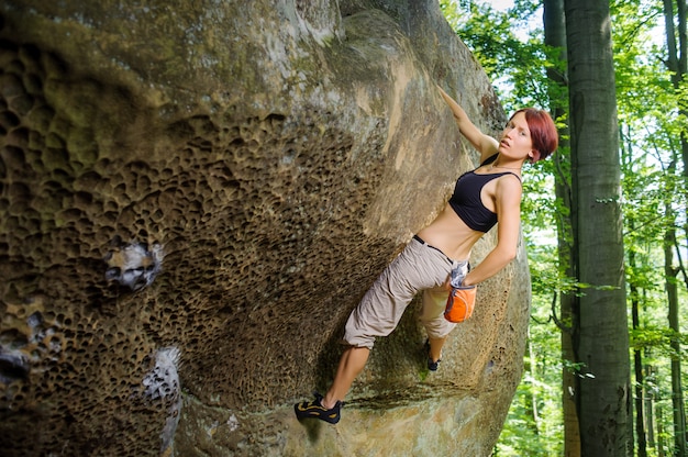 Rock-climber op grote rotsblok, opknoping op een hand