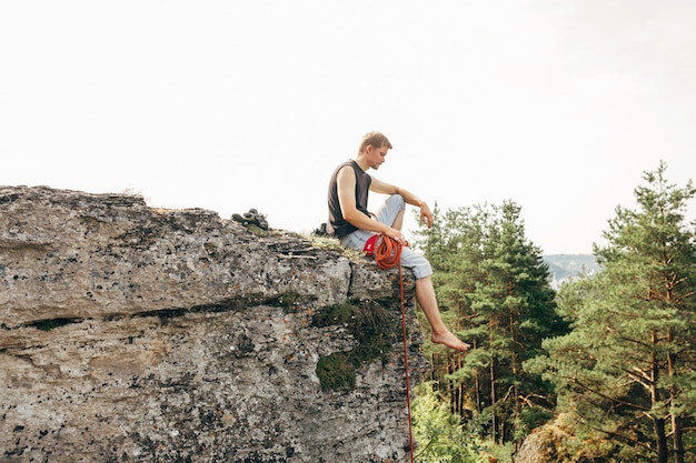 Rock climber sitting at the edge of the cliff with a rope