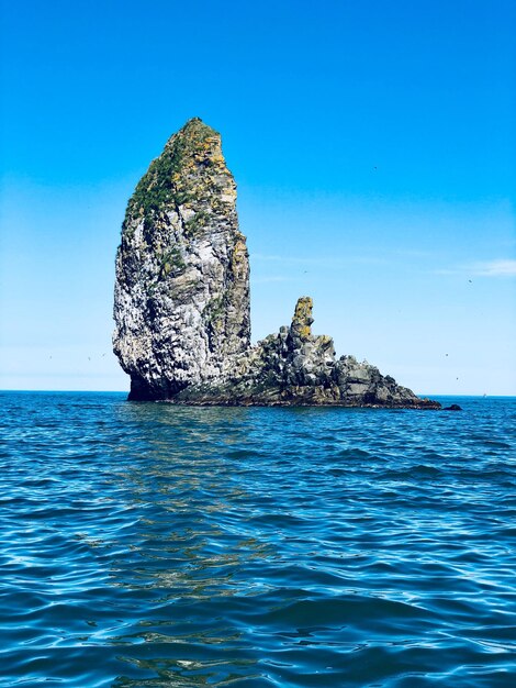 Rock formation in sea against clear blue sky