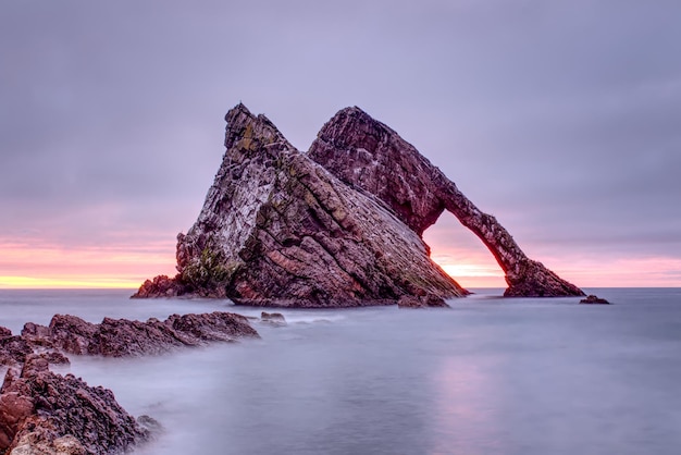 Rock formation in sea against sky during sunset