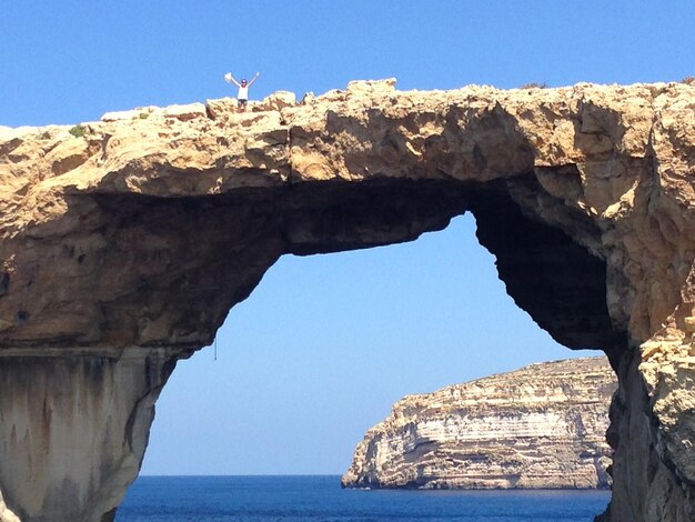 Rock formations by sea against clear blue sky