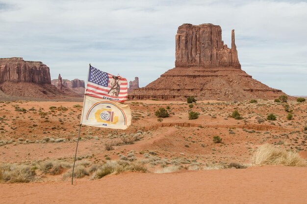 Photo the rock formationsof the monument valley in a desert with the american flag and the navajo flag