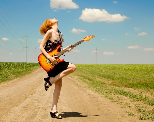 Rock girl with guitar at countryside.