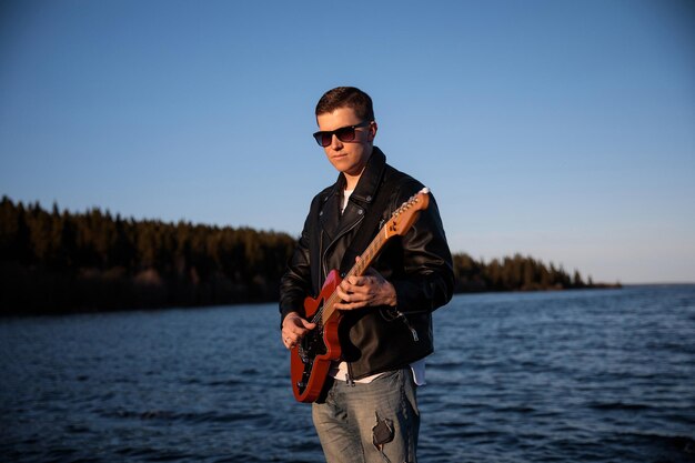 Rock guitarist plays the electric guitar against the backdrop of nature a lake on the background