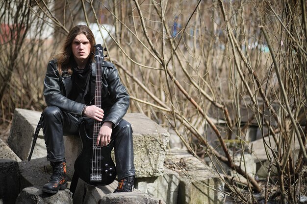 Photo rock guitarist on the steps a musician with a bass guitar in a leather suit metalist with a guitar on the background of industrial steps