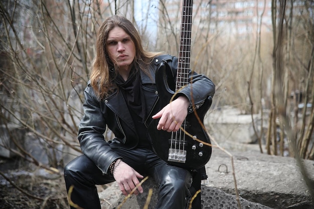 Rock guitarist on the steps A musician with a bass guitar in a leather suit Metalist with a guitar on the background of industrial steps