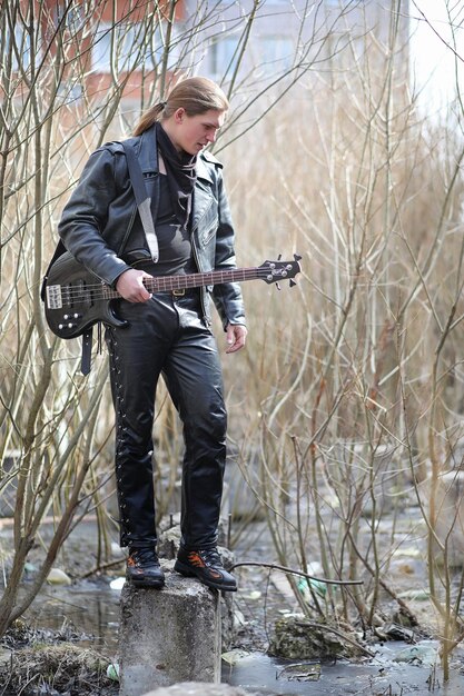 Photo rock guitarist on the steps a musician with a bass guitar in a leather suit metalist with a guitar on the background of industrial steps