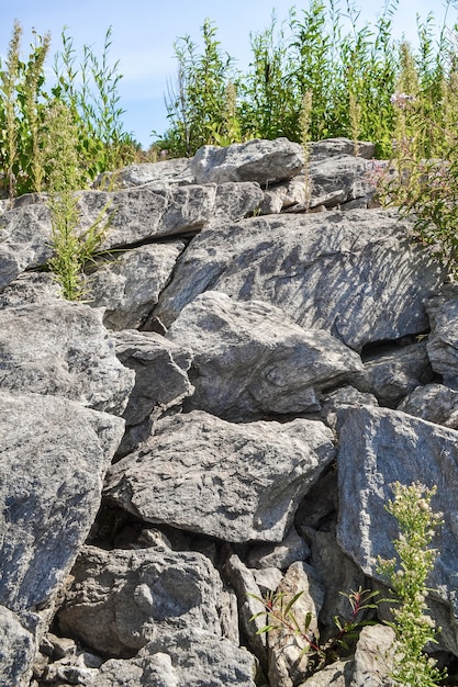 a rock of large stones and tall grass against a blue sky