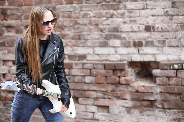A rock musician girl in a leather jacket with a guitar