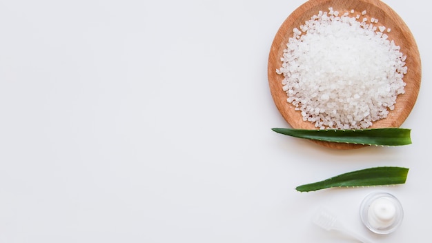 Foto salgemma sul piatto di legno con foglie di aloevera e foglie di idratante su sfondo bianco