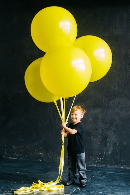 Rock star boy with a big yellow balloons. stylish baby on a\
black background.