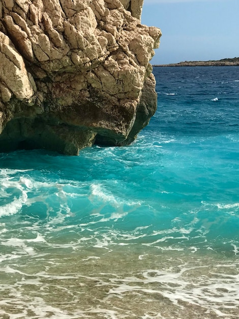 A rock in the water with the turquoise sea in the background