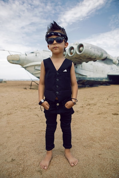 Rocker boy een kind in zwarte kleren staat tegen de achtergrond van een verlaten vliegtuig op het strand