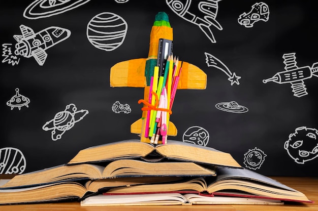 Rocket placed over a book in front of a blackboard depicting space objects in the classroom