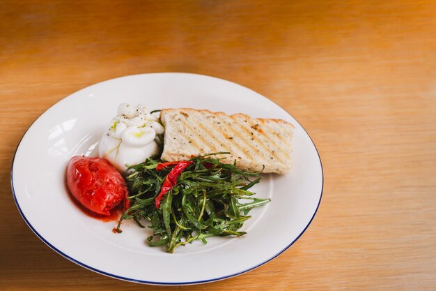 Rocket salade met Italiaanse burrata kaas en tomaten op een wit bord