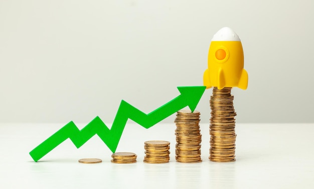 Rocket and stack of gold coins on a background of growing up chart with a green arrow Profit growth