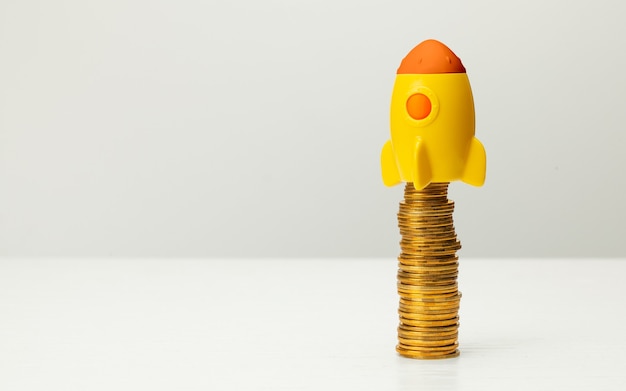 Rocket and stack of gold coins on gray background.