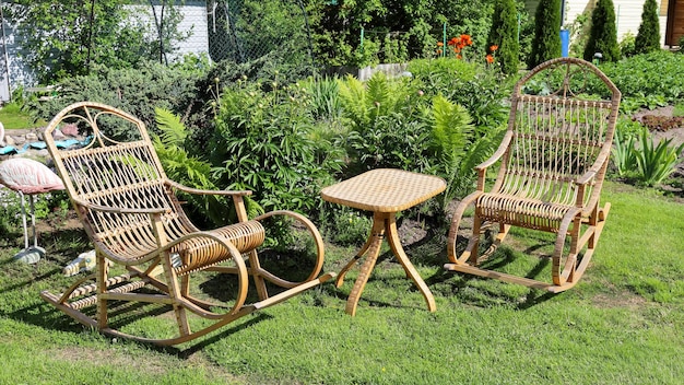 Rocking chair for recreation from rattan and small wicker table\
near flower bed