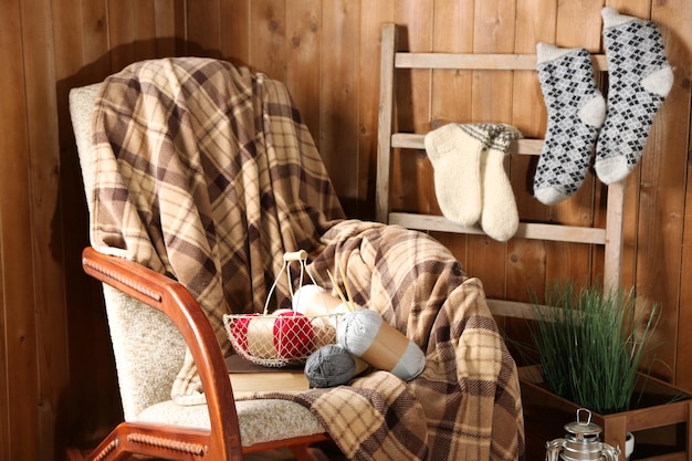 Rocking chair with plaid and yarn for knitting near wooden wall