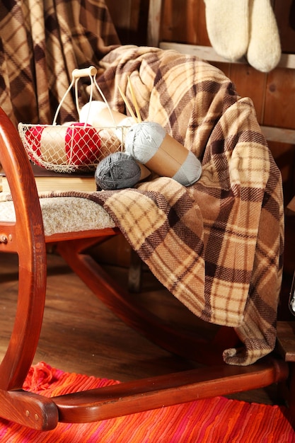 Photo rocking chair with plaid and yarn for knitting near wooden wall