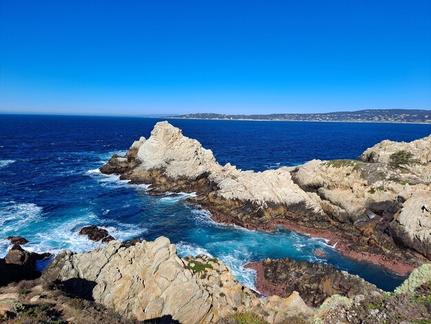 Rocks by sea against clear blue sky