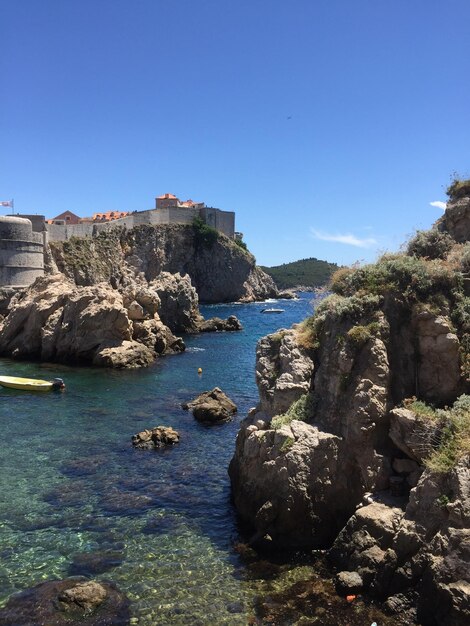 Rocks by sea against clear blue sky