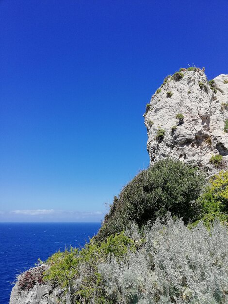 Rocks by sea against clear blue sky