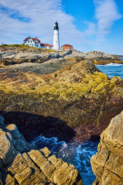 Rocks and ocean waves near white lighthouse in Maine