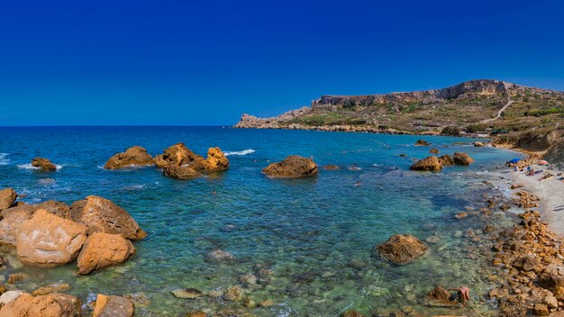 Rocks in sea against clear blue sky