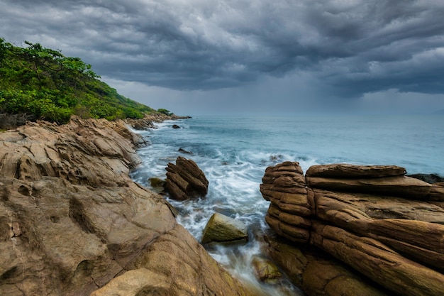 写真 雨の前に水が当たる岩の多いビーチ