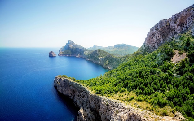 a rocky cliff with a view of a bay and a mountain in the background