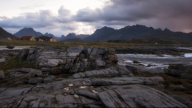 山と漁村を背景にしたロフォーテン諸島のノルウェーの北海の岩の多い海岸