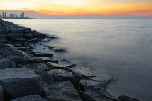 The rocky coastline with flowing water in the motion and the City in Thailand