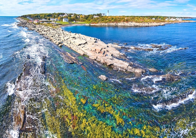 Rocky coastline with shallow waters and waves crashing in Maine and lighthouses in distance