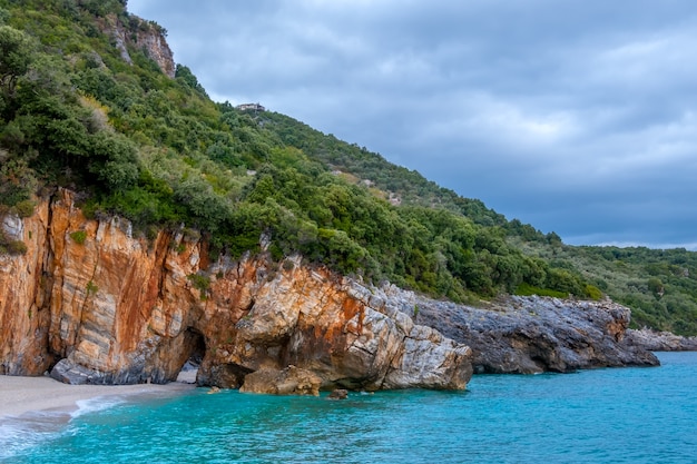 Riva della foresta rocciosa del mare in tempo nuvoloso. villa sul pendio. c'è un arco in pietra naturale sulla spiaggia