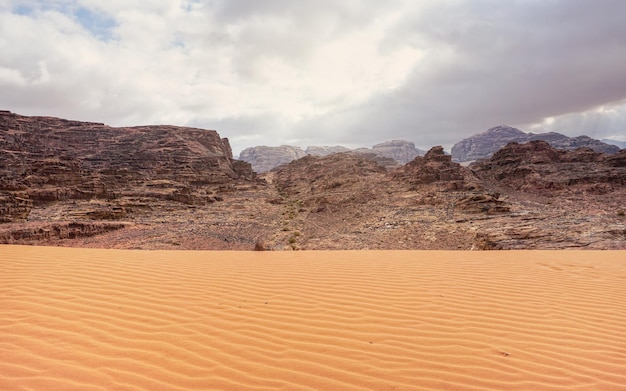 Rocky massifs on red desert, patterns on small sand dunes in foreground, typical scenery in Wadi Rum, Jordan