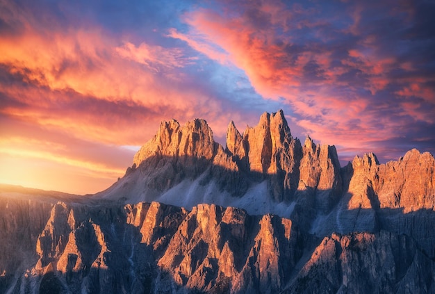 Foto montagne rocciose al tramonto colorato incredibile in estate nelle dolomiti italia creste montuose e bel cielo con nuvole rosa rosse e ornate e luce solare in primavera paesaggio con picco di montagna di rocce