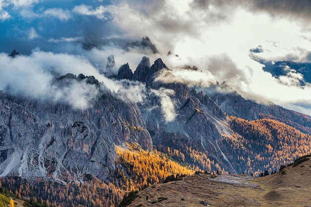 Rocky mountains covered with clouds and colorful trees in autumn season, Dolomite alps, Italy