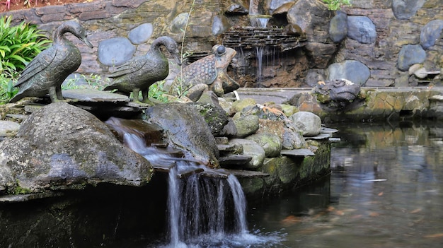 A rocky pond with a mini waterfall with some animal statues