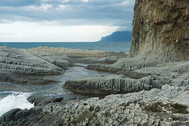 Rocky seashore formed by columnar basalt against the backdrop of a stormy sea coastal landscape of the Kuril Islands