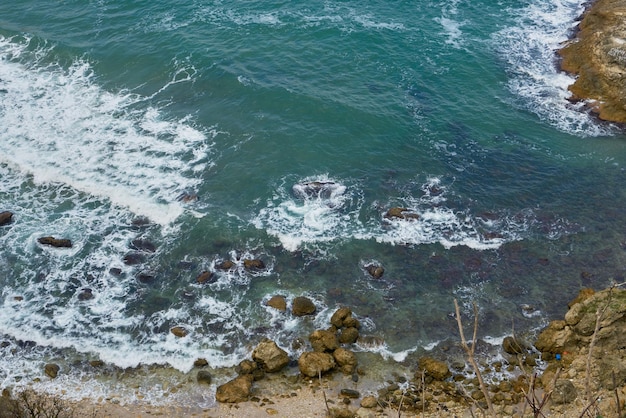 Rocky seaside cliff with white waves.