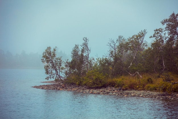 Rocky shore of mountain lake in misty autumn morning Beautiful nature Norway Reflection on the lake