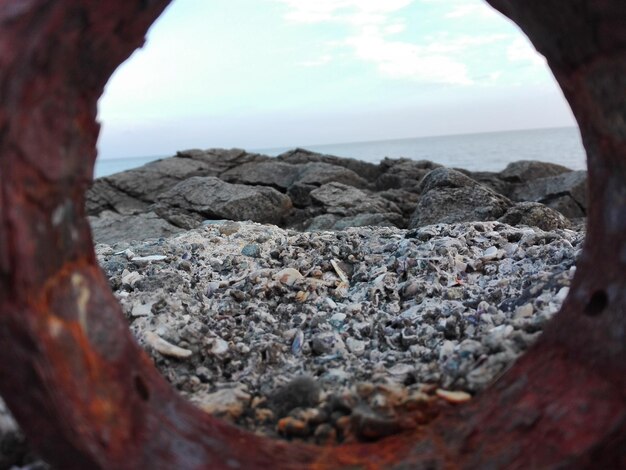 Photo rocky shore at sea against sky seen through rusty metal