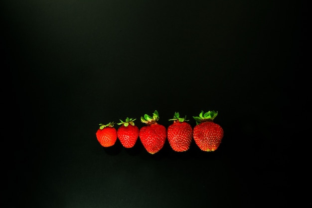 Rode aardbei op zwarte achtergrond. rode aardbeien in een lijn