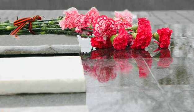Rode anjerbloemen liggen op een regenachtige dag op het grijze marmer van het monument