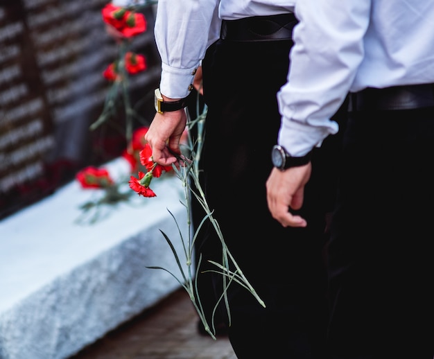 Rode anjers in de handen van mannen in zwarte broeken en witte overhemden die naar het monument gaan om te eren. De zeelieden.