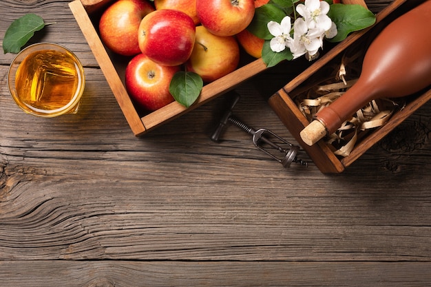 rode appels in houten kist met tak, glas en fles cider op een houten tafel.